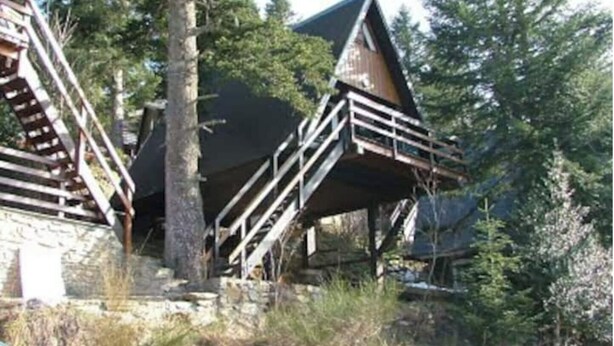 A rustic cabin with a wooden staircase leading to a deck, surrounded by trees. - Chalet Guzet Snow (Seix)