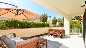 Eine Terrasse im Freien mit Holzmöbeln, einem gemusterten Teppich und einem großen Sonnenschirm.