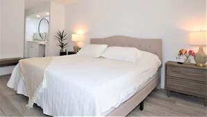 Ein großes Bett mit Kopfteil, zwei Nachttische mit Lampen, eine Kommode und ein Spiegel im Schlafzimmer.