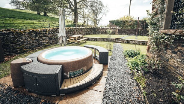 A hot tub with a wooden deck, surrounded by a stone wall and a garden. - Luxurious Cottage with Hot Tub. 19 miles from Windermere. (Sedbergh)