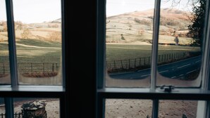 A view through a window of a rural landscape with rolling hills, a road, and a fence. - Luxurious Cottage with Hot Tub. 19 miles from Windermere. (Sedbergh)