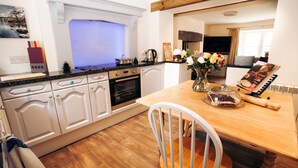 A modern kitchen with white cabinets, a wooden countertop, and a dining area with a wooden table and a chair. - Luxurious Cottage with Hot Tub. 19 miles from Windermere. (Sedbergh)