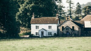 A white house with a stone extension, surrounded by a grassy field and trees. - Luxurious Cottage with Hot Tub. 19 miles from Windermere. (Sedbergh)