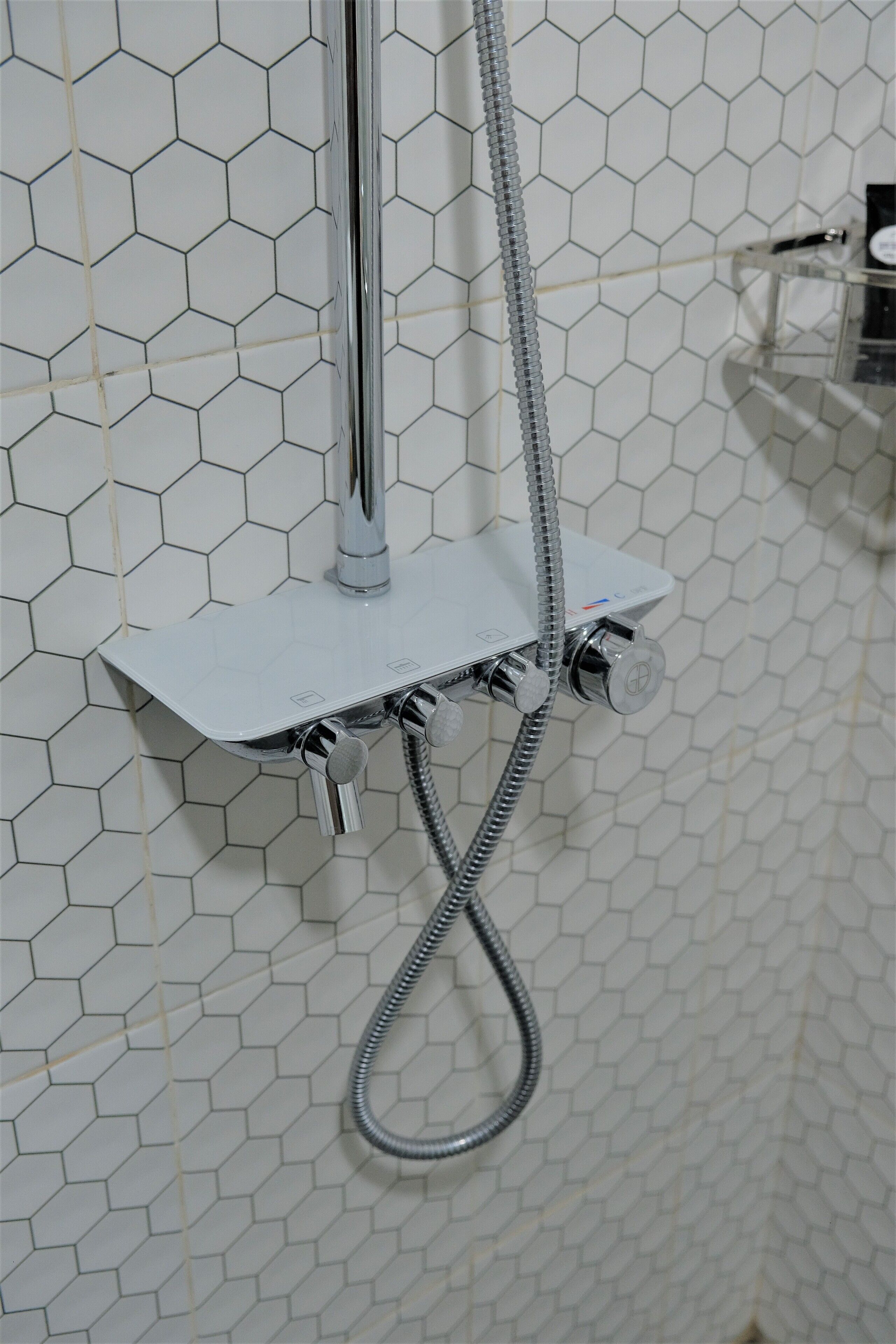 A shower with a chrome faucet and hose, mounted on a white hexagonal tile wall.