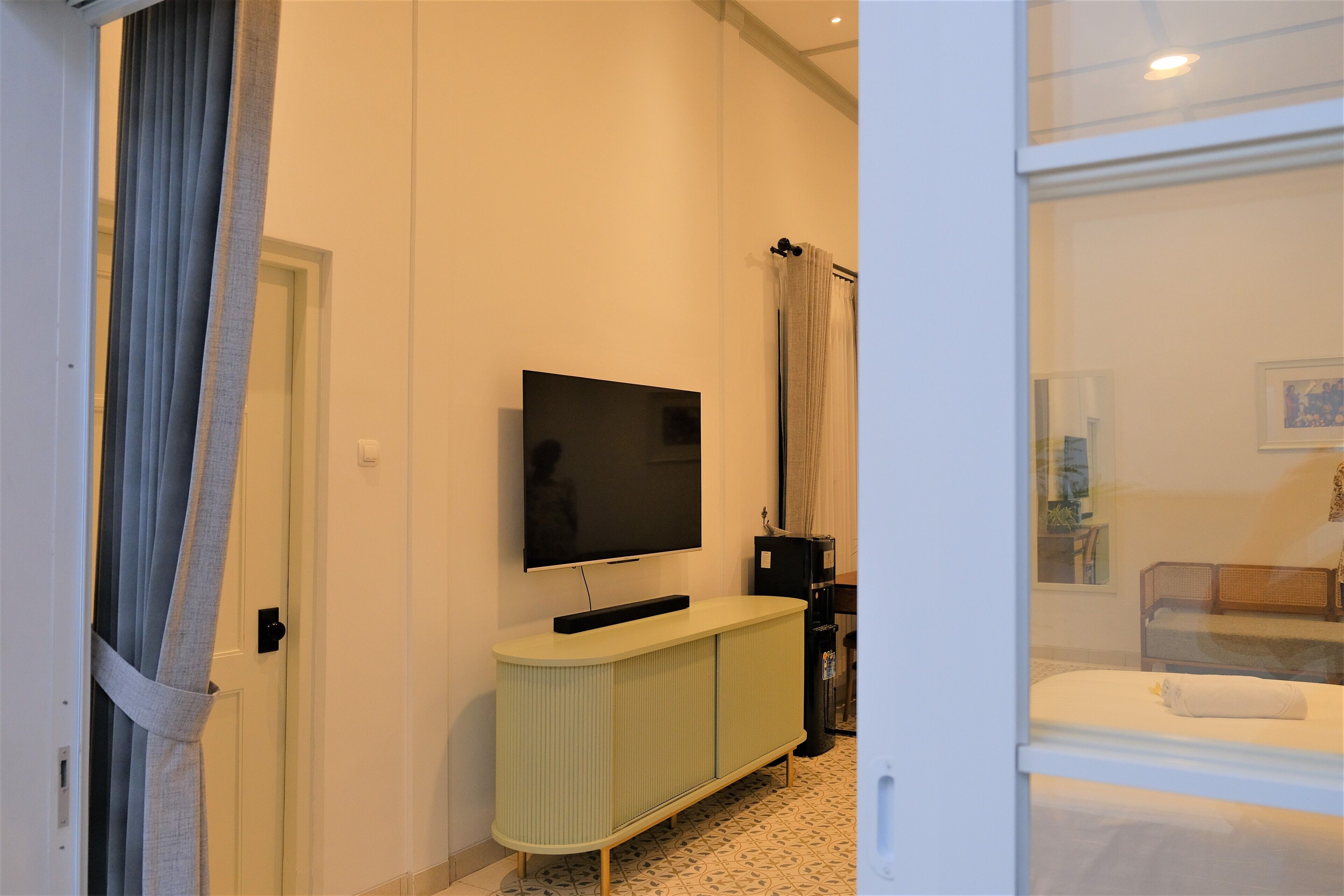 A hotel room with a television mounted on the wall, a light-colored cabinet, and a bed with a white blanket.