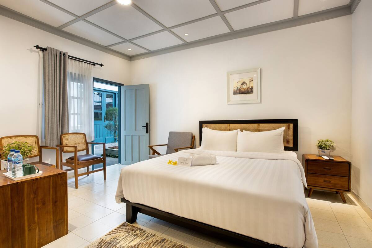 Hotelkamer met een groot bed, een bureau met een plant, een stoel, een nachtkastje en uitzicht op de omgeving.