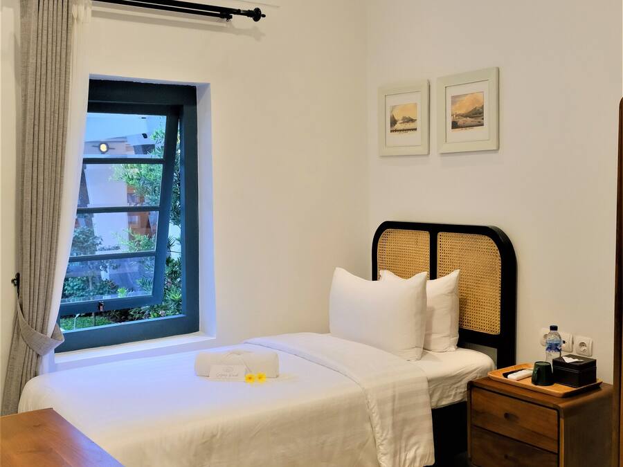 Een hotelkamer met een bed, een houten nachtkastje, een raam met gordijnen en twee foto's in lijsten aan de muur.