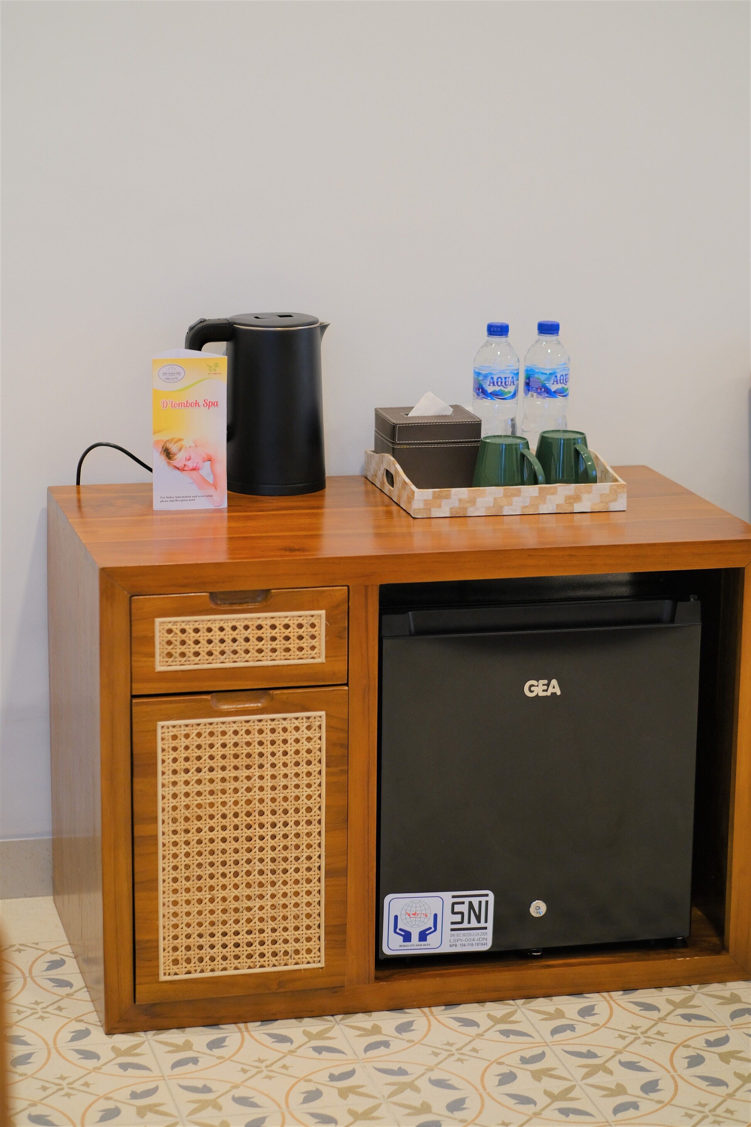 A compact minibar with a GEA refrigerator, a black coffee maker, two water bottles, and a tissue box.