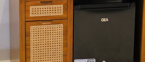 A compact minibar with a GEA refrigerator, a black coffee maker, two water bottles, and a tissue box.