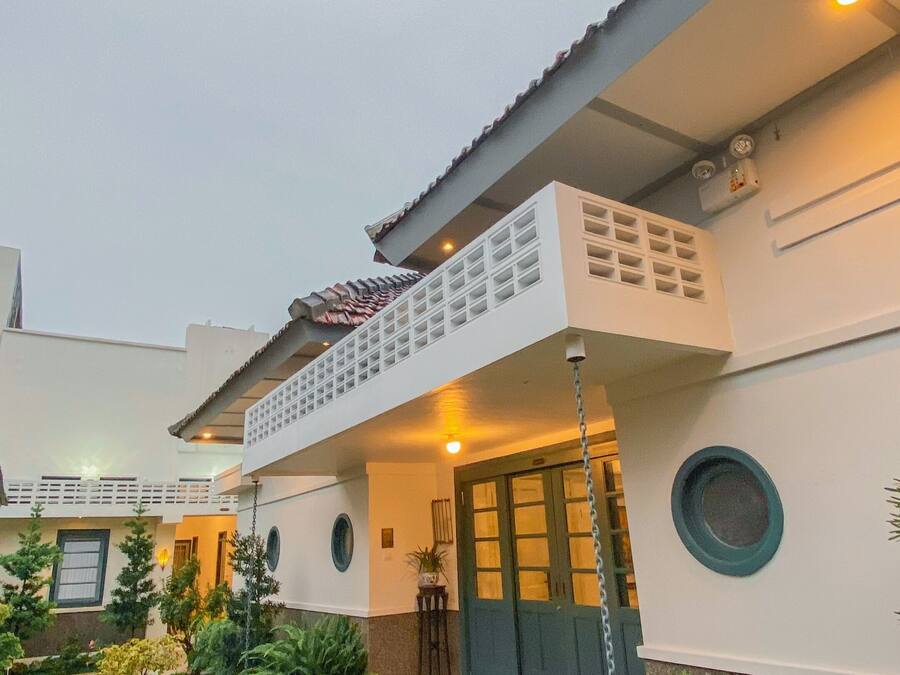A modern house with a balcony, a front door, and a garden with potted plants.