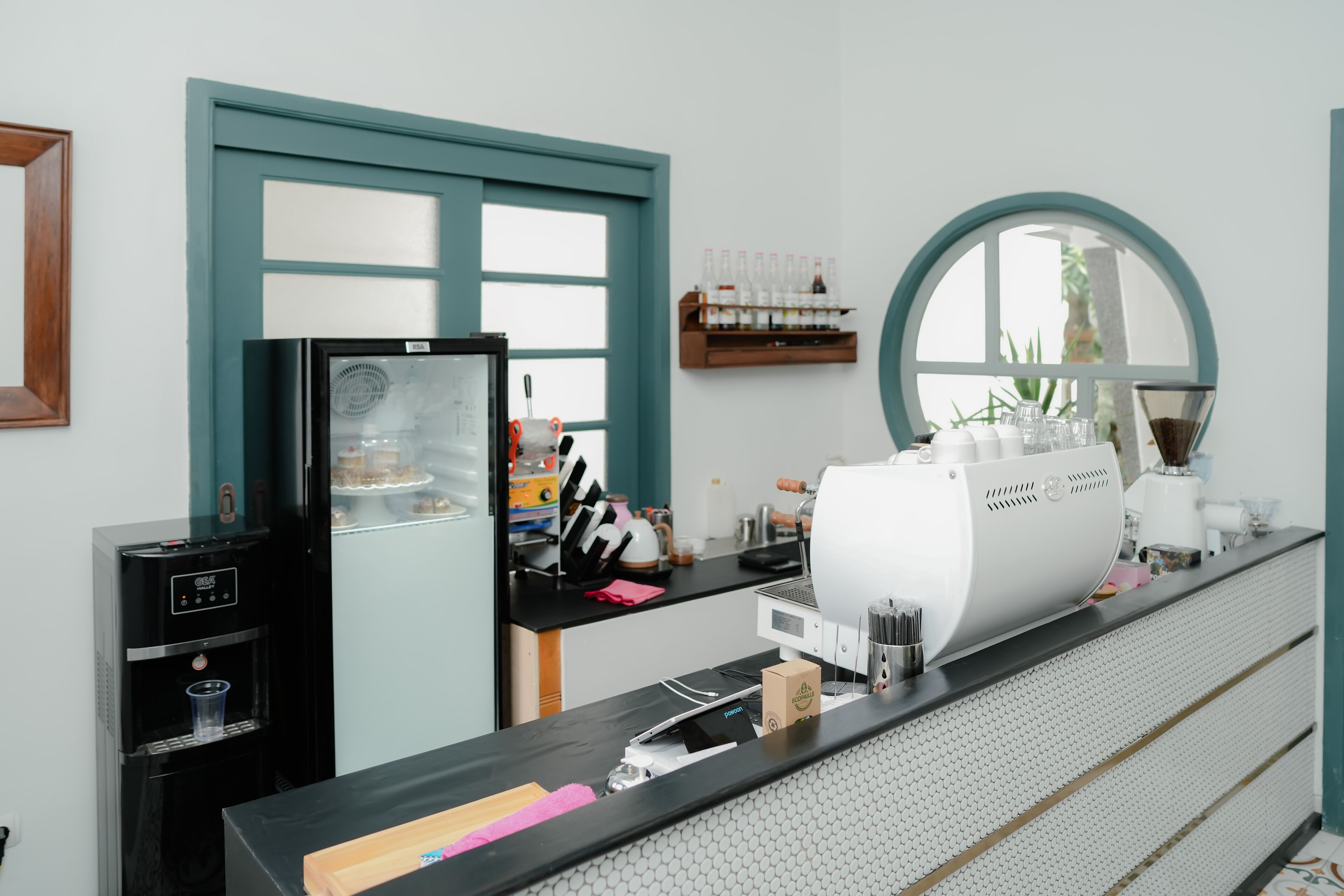 A kitchen with a coffee machine, a water dispenser, and a shelf with bottles.