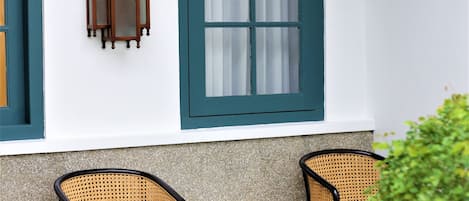 A room with a white wall, a window with green trim, two wicker chairs, and a small table.