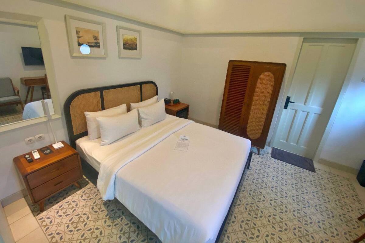 Een hotelkamer met een groot bed, een nachtkastje met een lamp, een houten hoofdeinde en een deur met een louwerdesign.