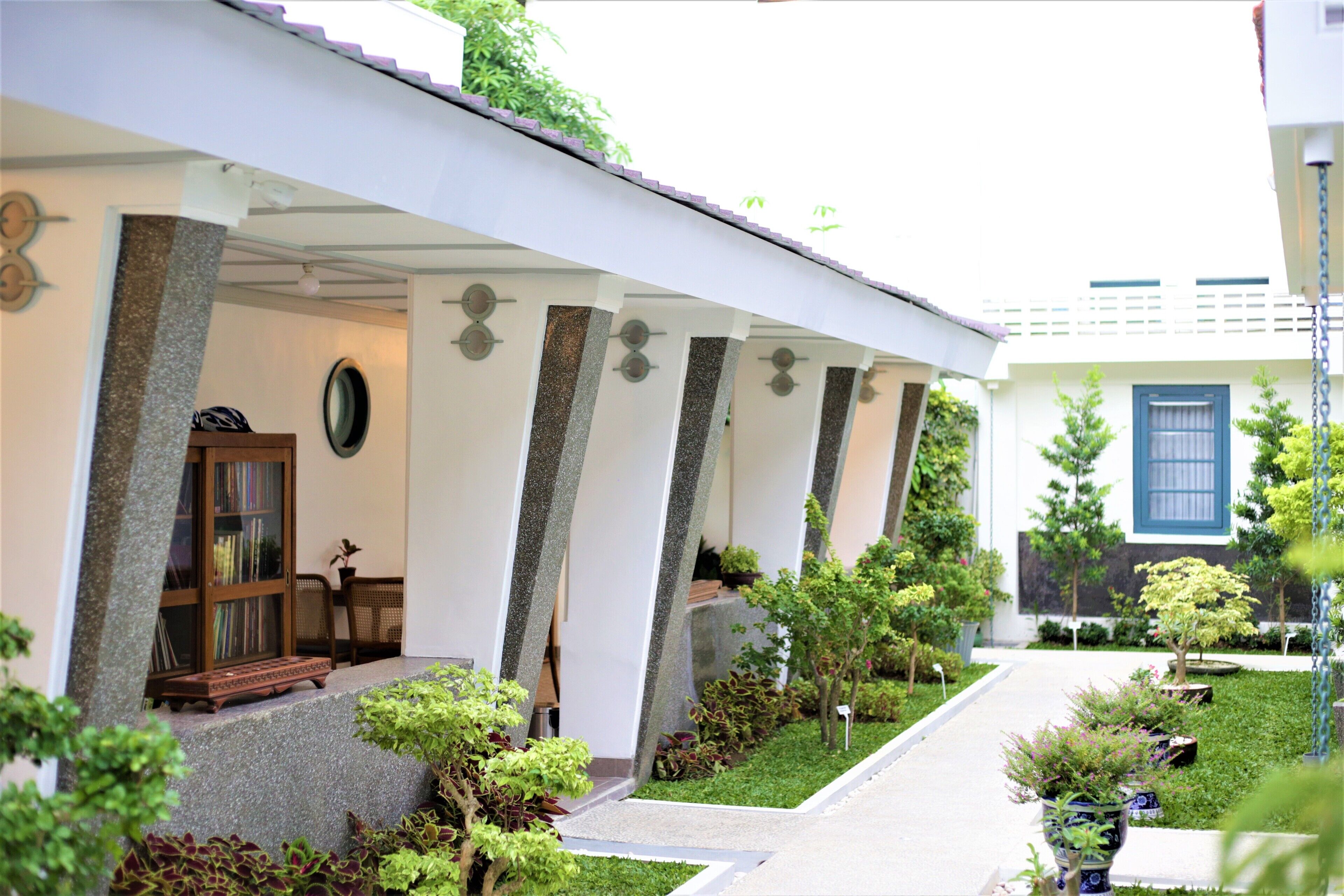 A building with a covered porch, columns, a bookshelf, and a small garden with potted plants.