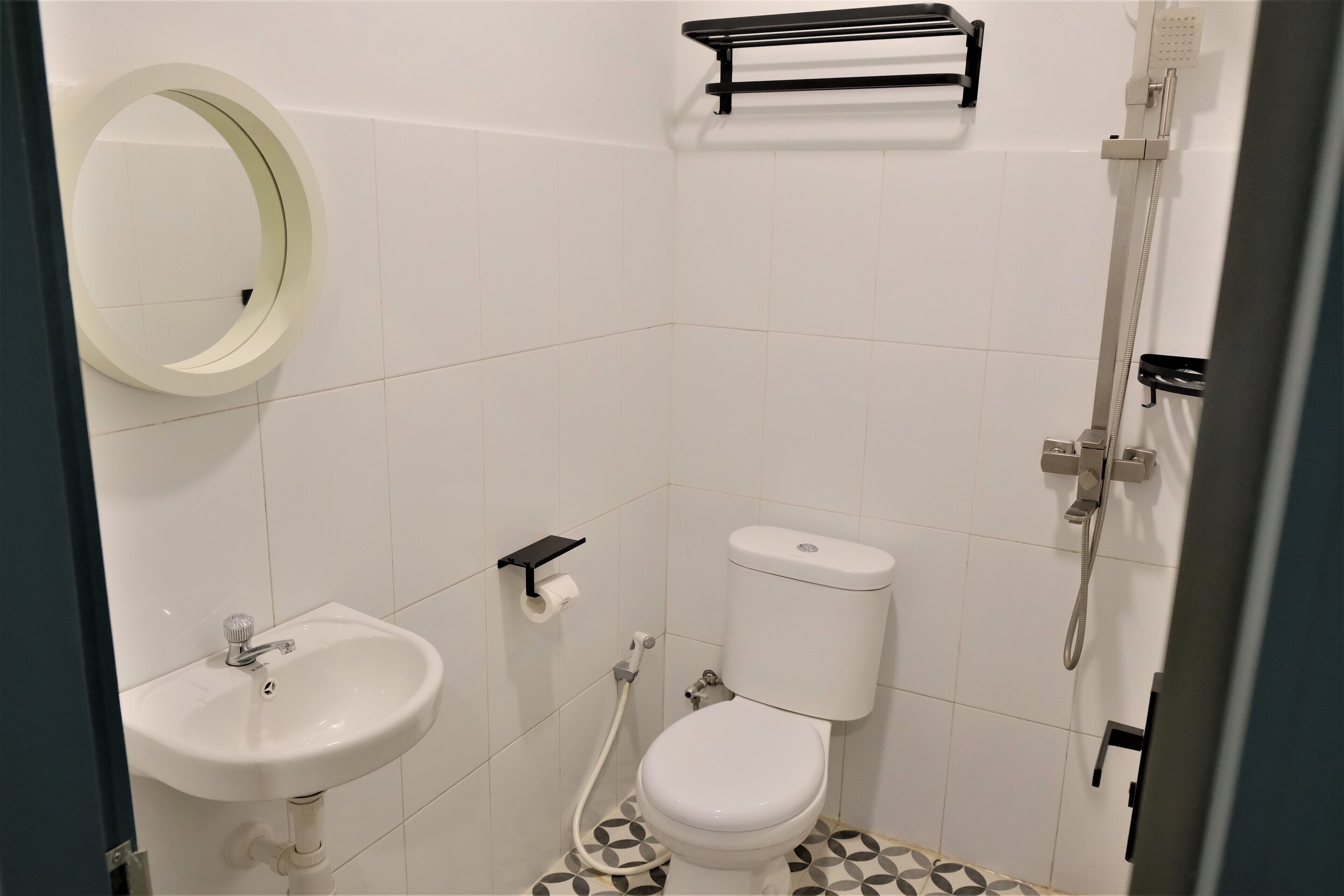 Une petite salle de bain moderne avec un lavabo, des toilettes et une douche, le tout de couleur blanche. On trouve un porte-serviettes au-dessus des toilettes et un miroir au mur.
