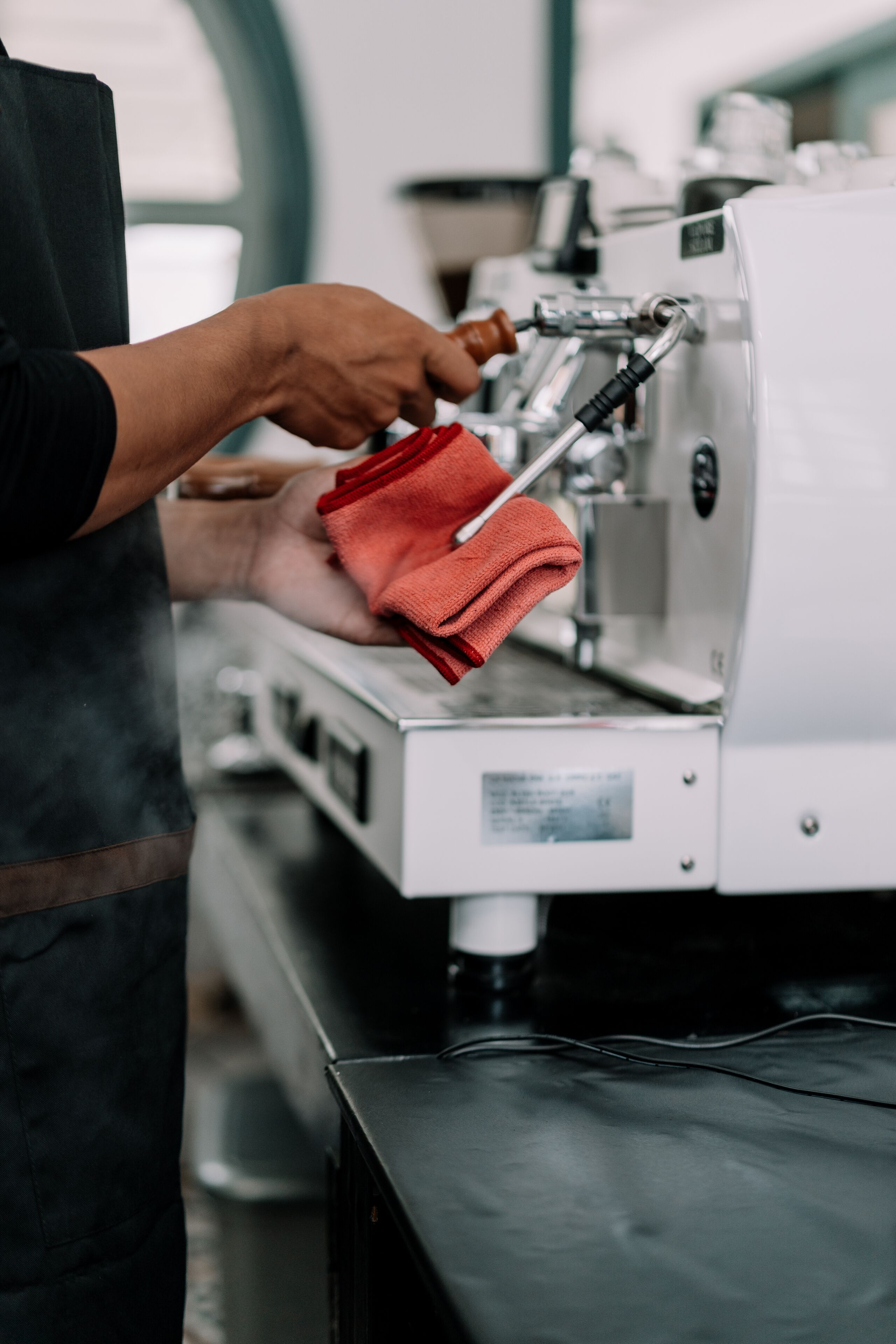 A person operating a coffee machine, with a focus on the machine's interface and a red cloth nearby.