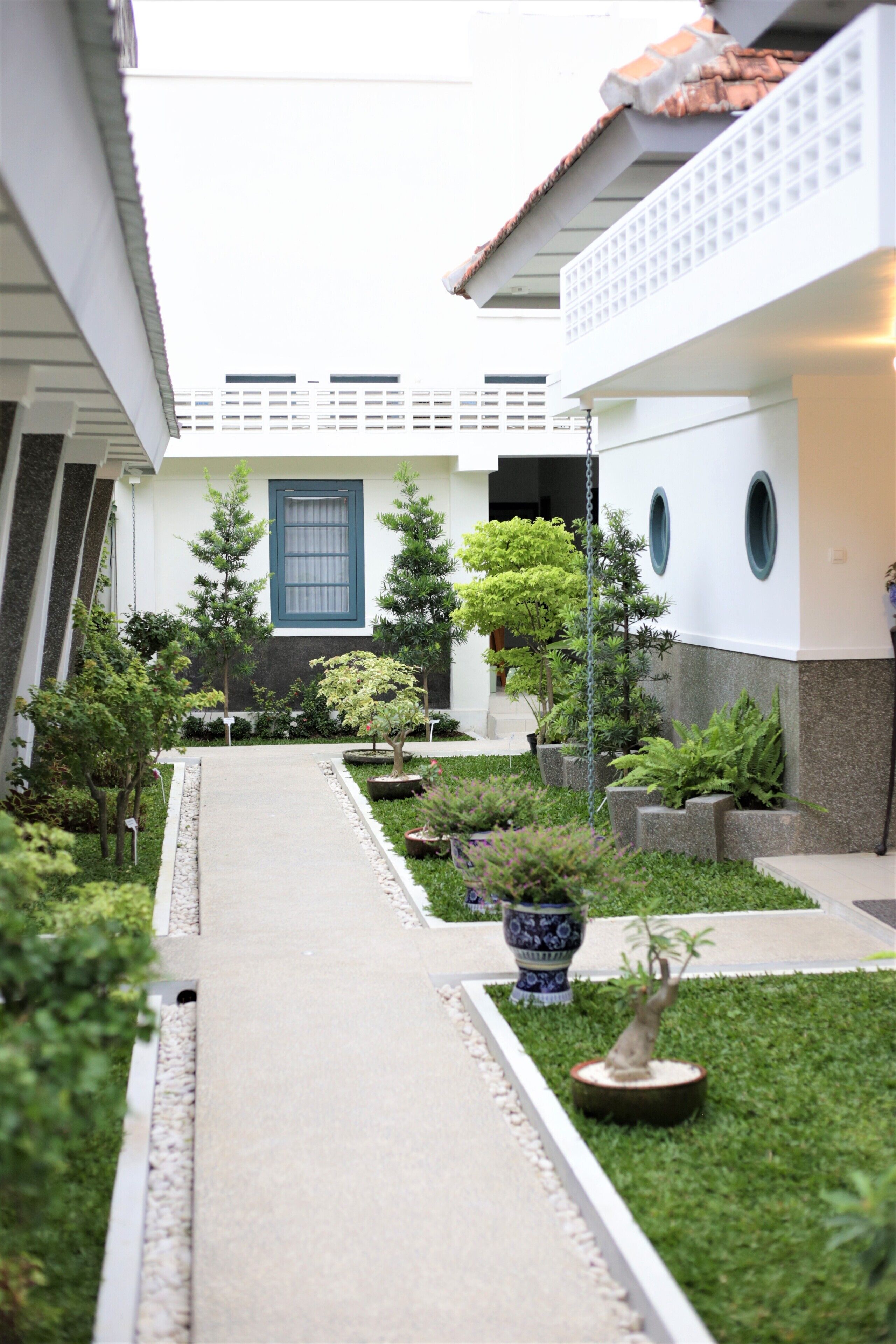 Un patio con un sendero, plantas en macetas y un edificio con ventanal azul y balcón.