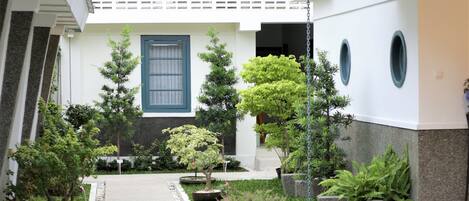 Un patio con un sendero, plantas en macetas y un edificio con ventanal azul y balcón.
