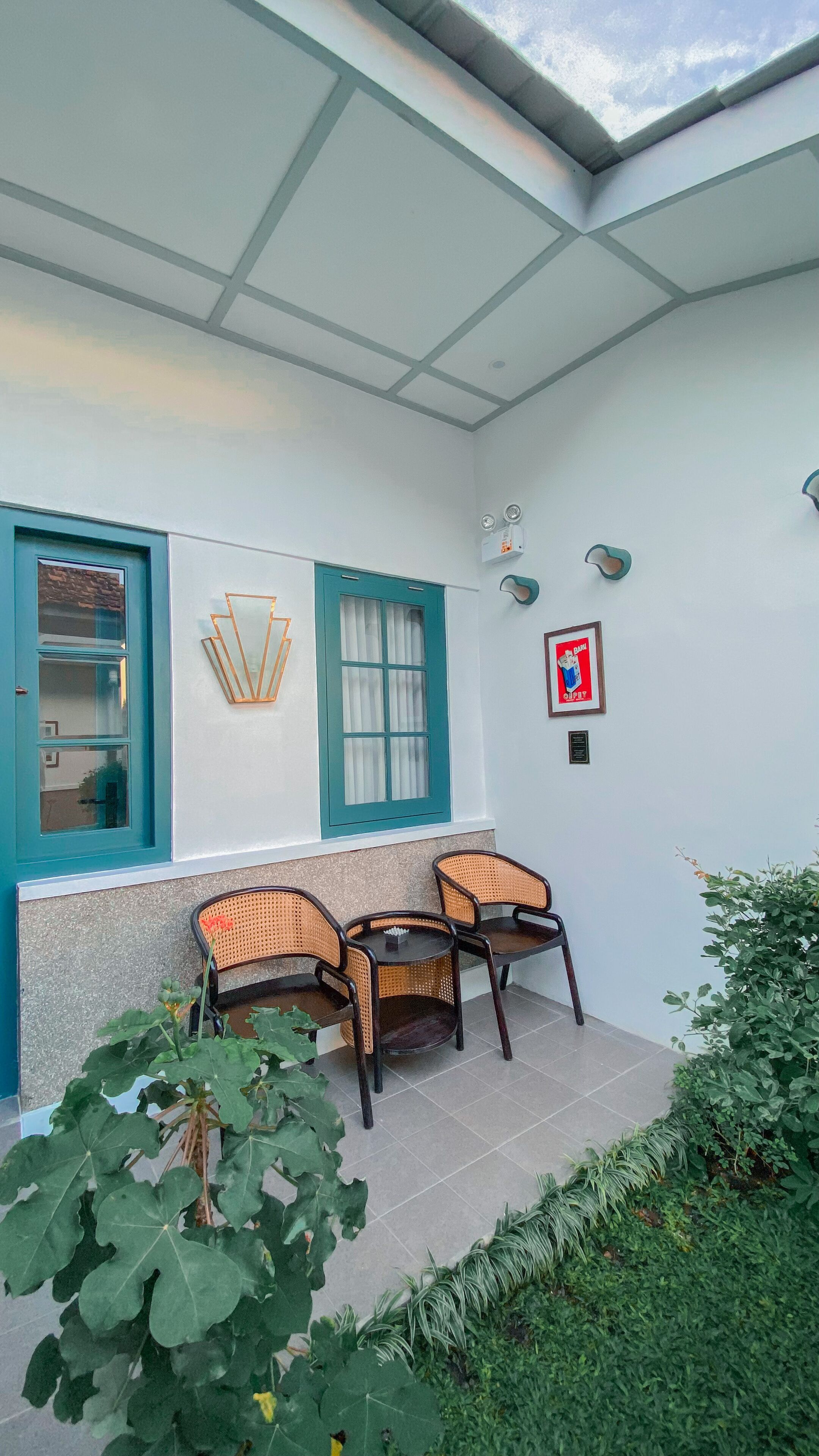 Un'area patio coperta con tre poltrone in vimini, una finestra con davanzali blu e un faretto a parete.