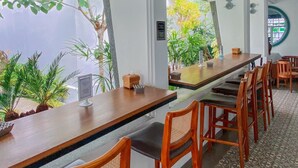 Een lange houten bar met hoge krukken, omringd door witte muren en grote ramen.