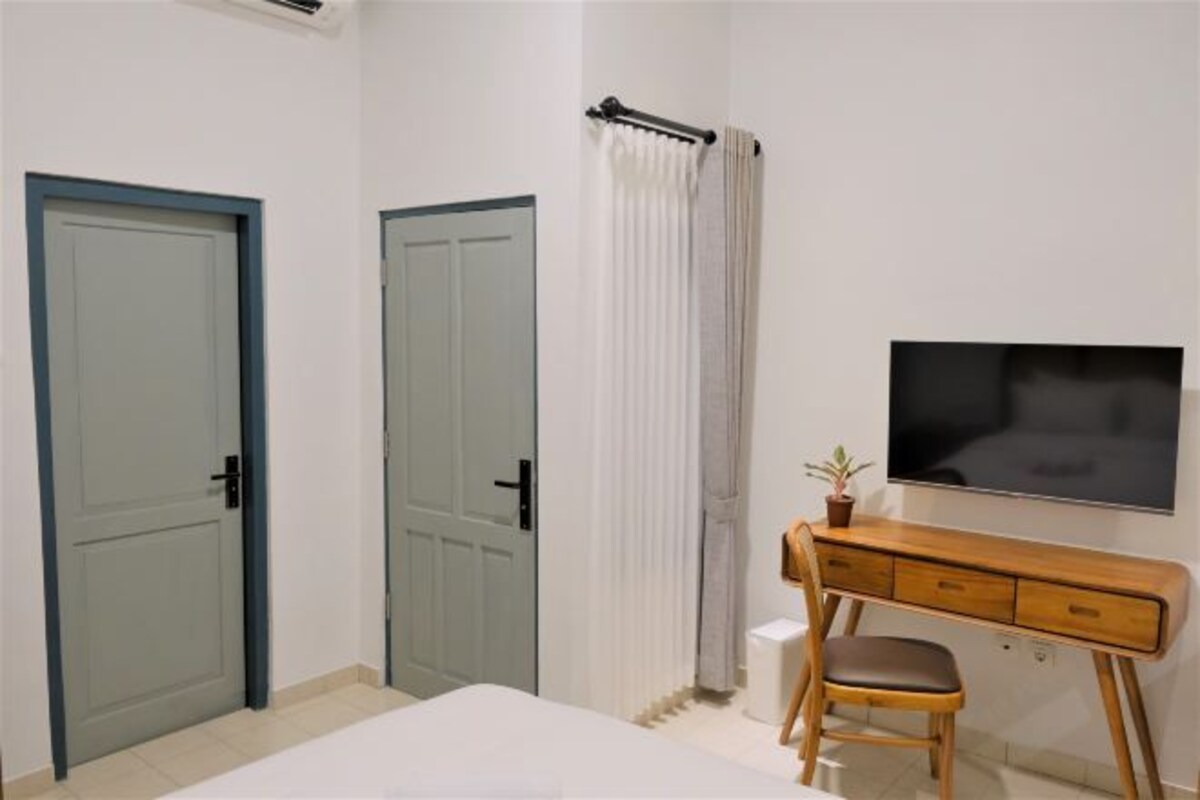 Een slaapkamer met een bed, een houten bureau met stoel, een televisie en twee deuren.