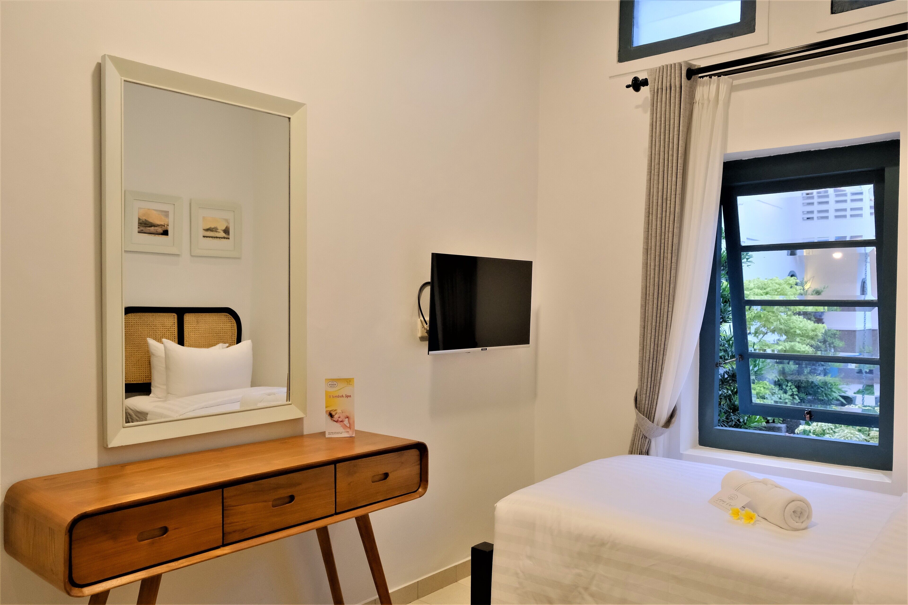 Quarto de hotel com cama, mesa de cabeceira de madeira com espelho, televisão de tela plana e janela com cortinas.