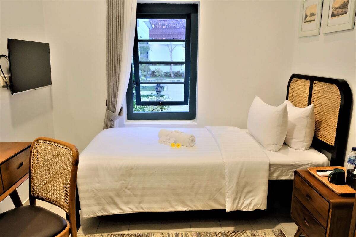Hotelkamer met een bed, bureau, stoel, raam met uitzicht en een aan de muur bevestigde flatscreen-tv.