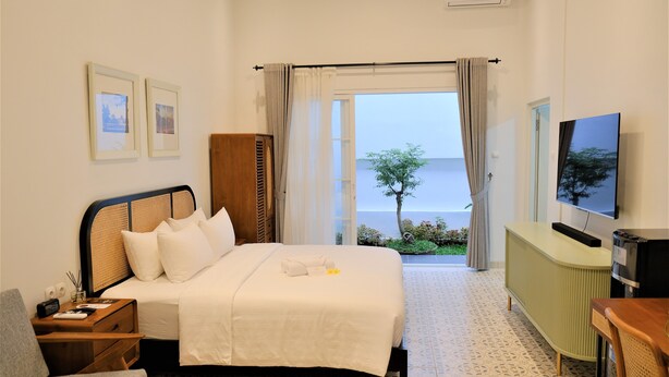 Een hotelkamer met een bed, een televisie, een bureau en uitzicht op zee.