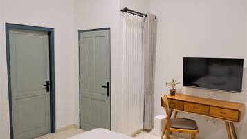A bedroom with a bed, a wooden desk, a chair, a TV, and two doors.