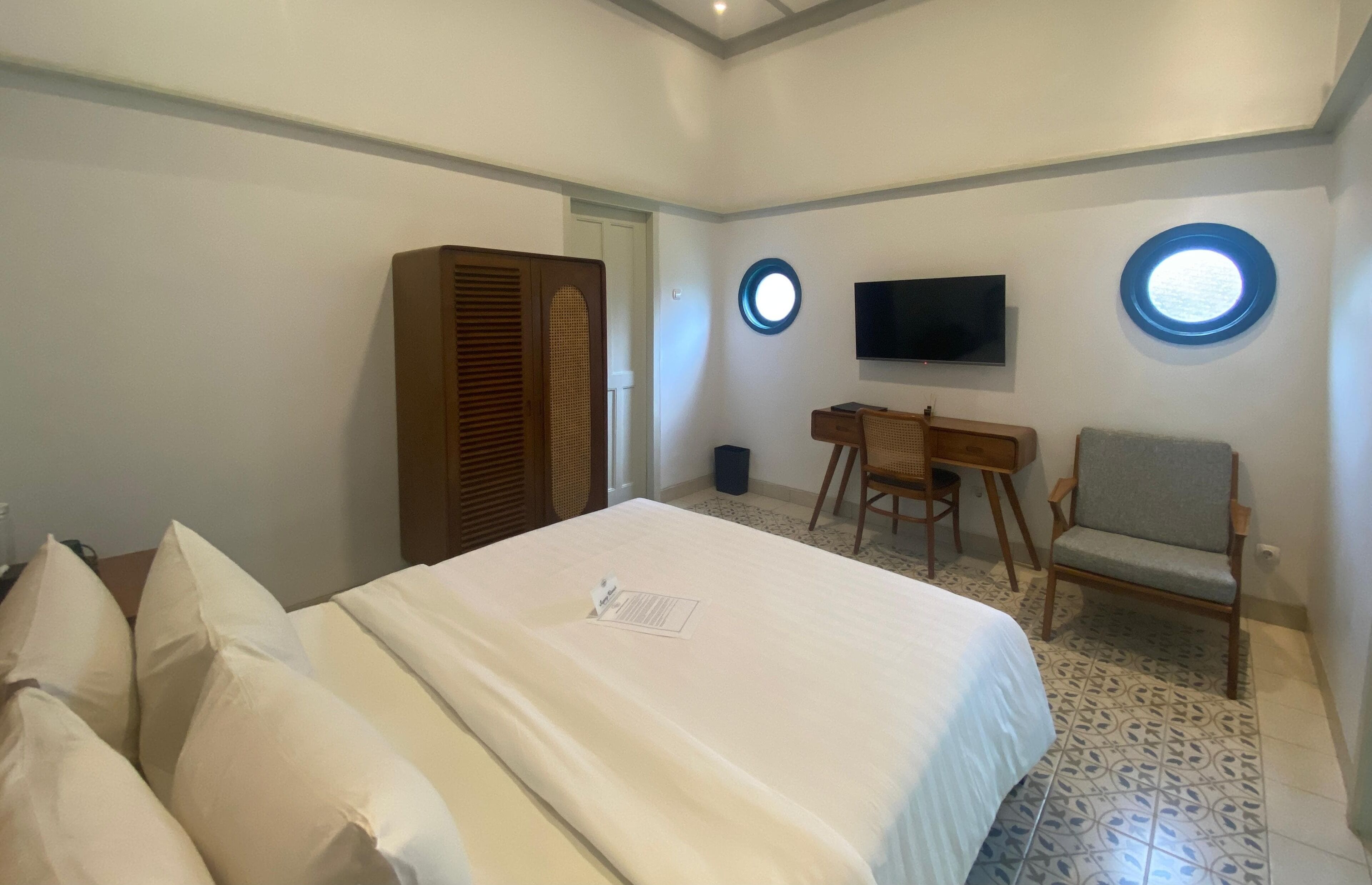 Ein Hotelzimmer mit einem Bett, einem Schreibtisch, einem Stuhl, einem Fernseher und zwei runden Fenstern an der Wand.