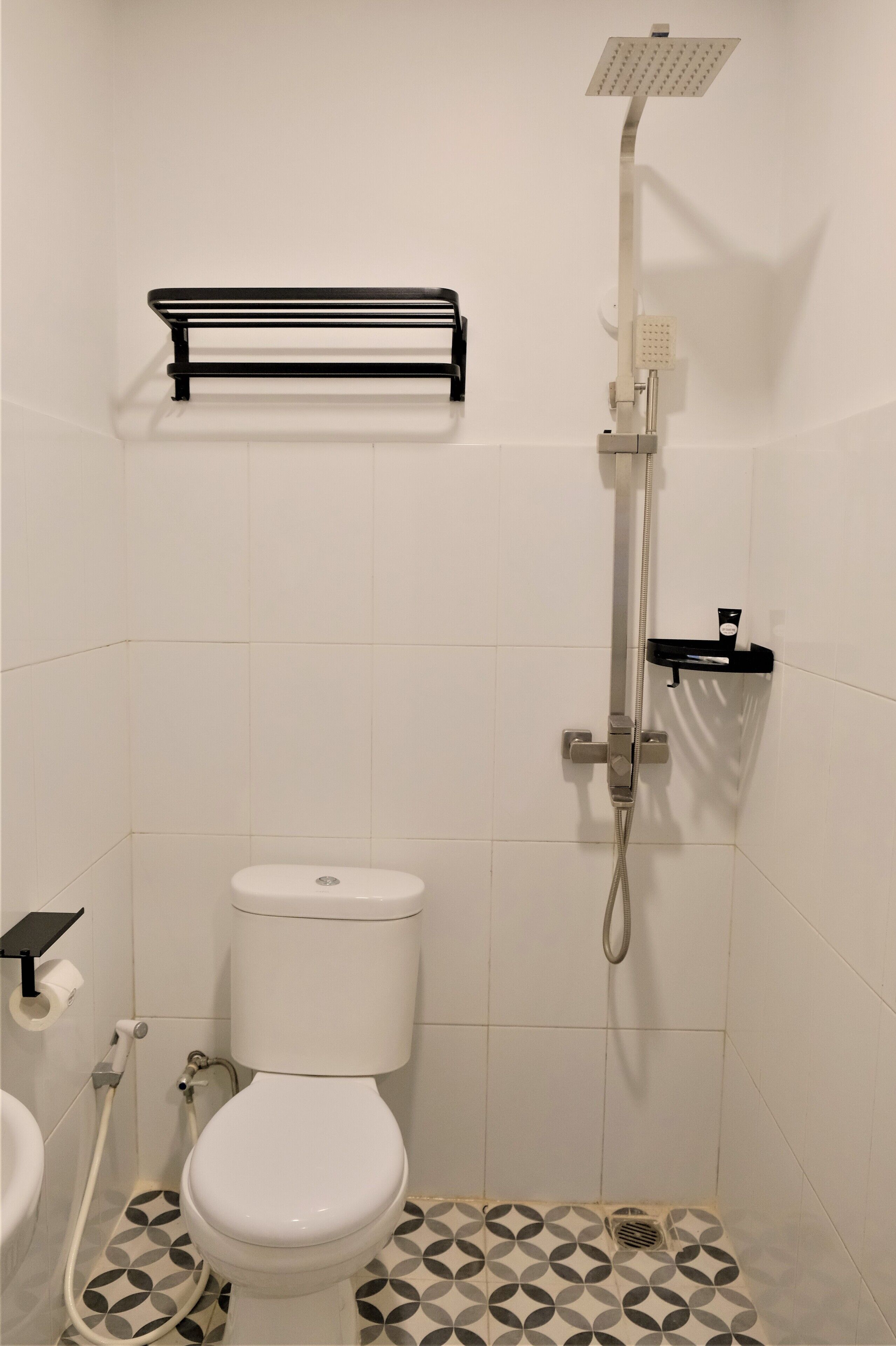 A bathroom with a toilet, a shower, and a black towel rack.