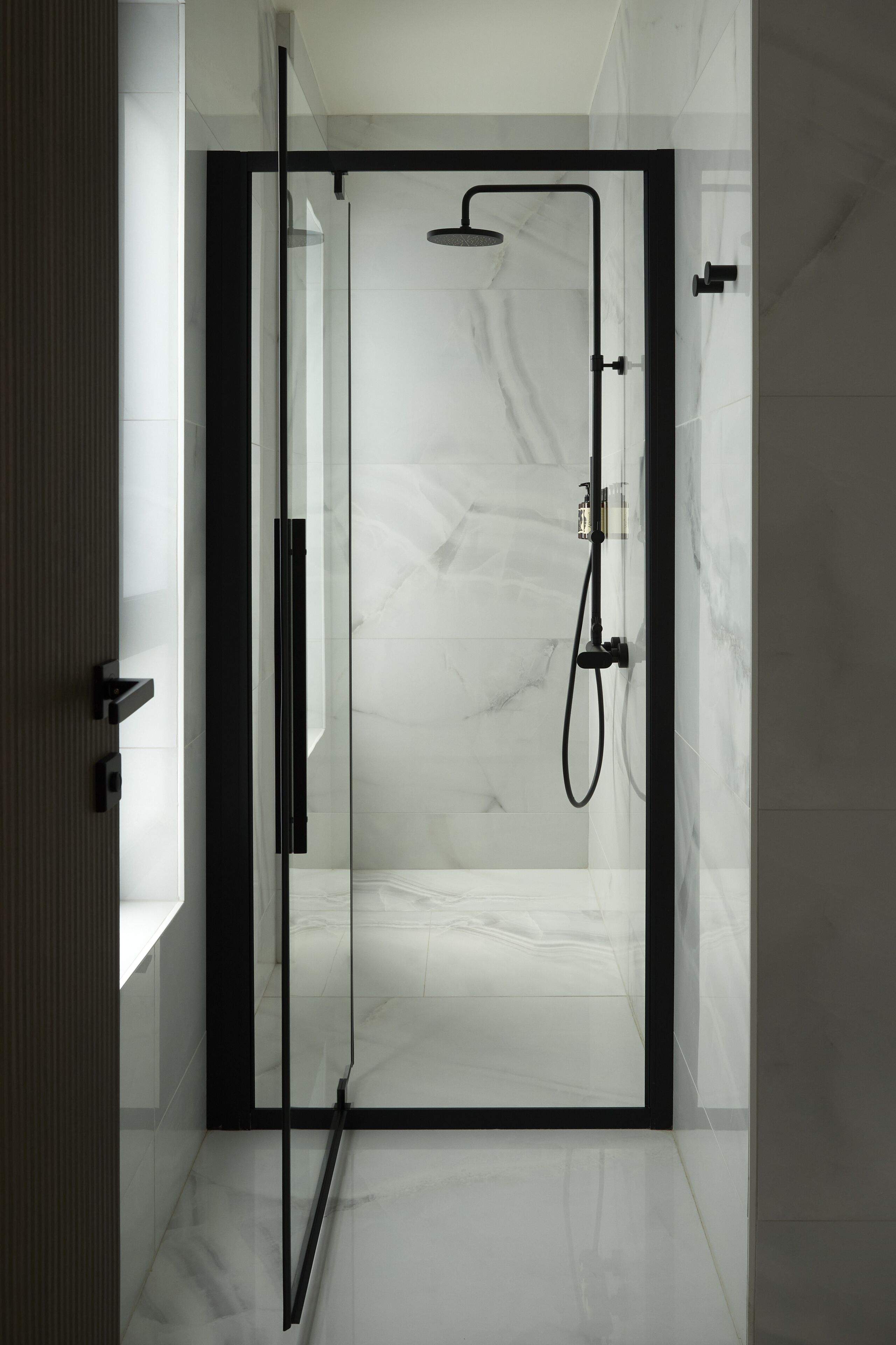 A modern bathroom with a glass door, a shower with a handheld showerhead, and a marble floor.