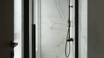 A modern bathroom with a glass door, a shower with a handheld showerhead, and a marble floor.