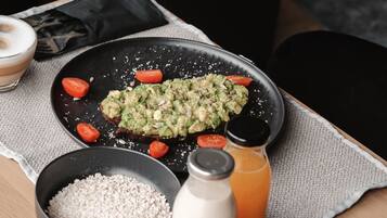 A breakfast setting with a plate of avocado toast, a bowl of oats, a glass of orange juice, and a bottle of milk on a table.