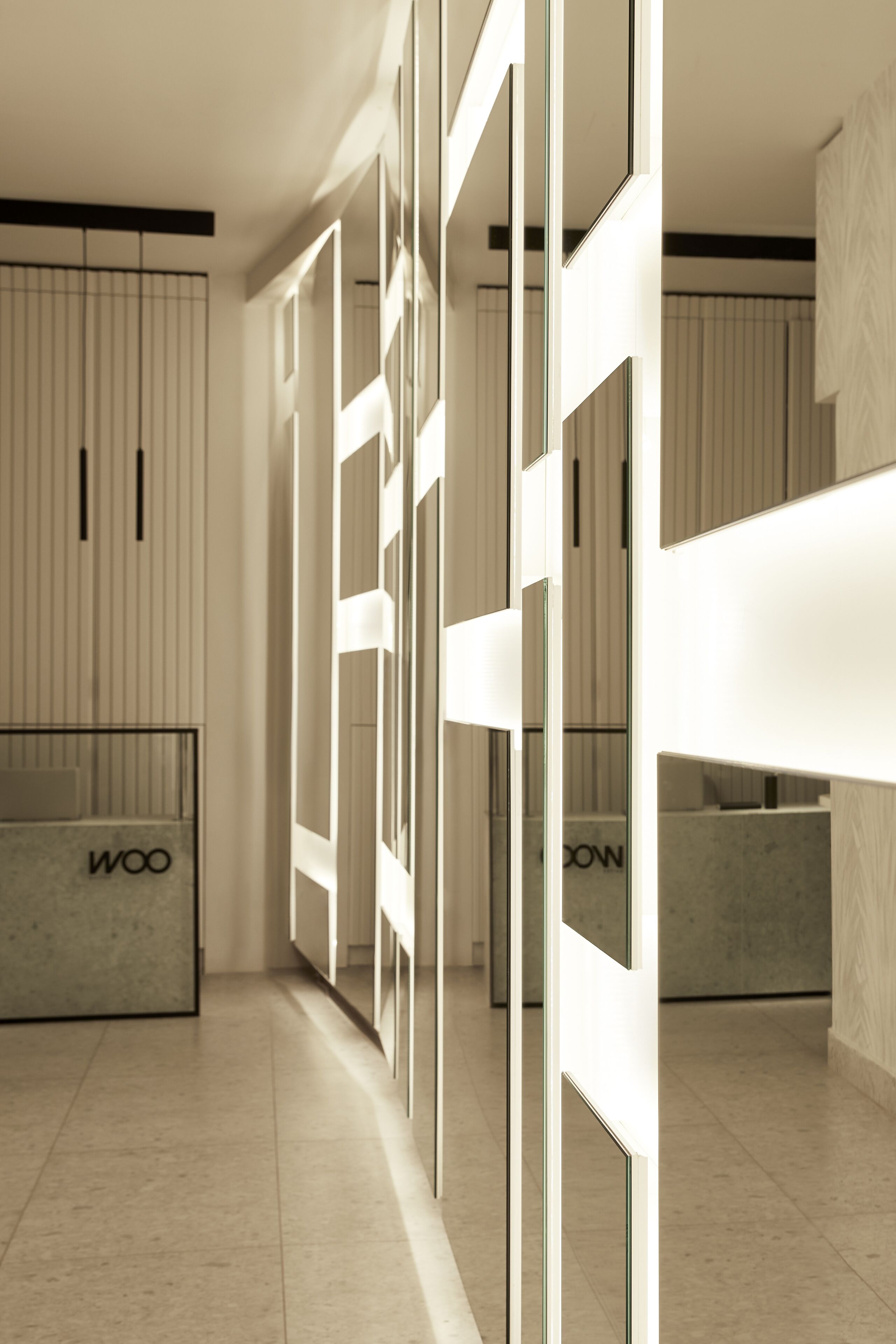 A modern hotel lobby with a minimalist design, featuring a reception desk, glass partitions, and a clean, tiled floor.