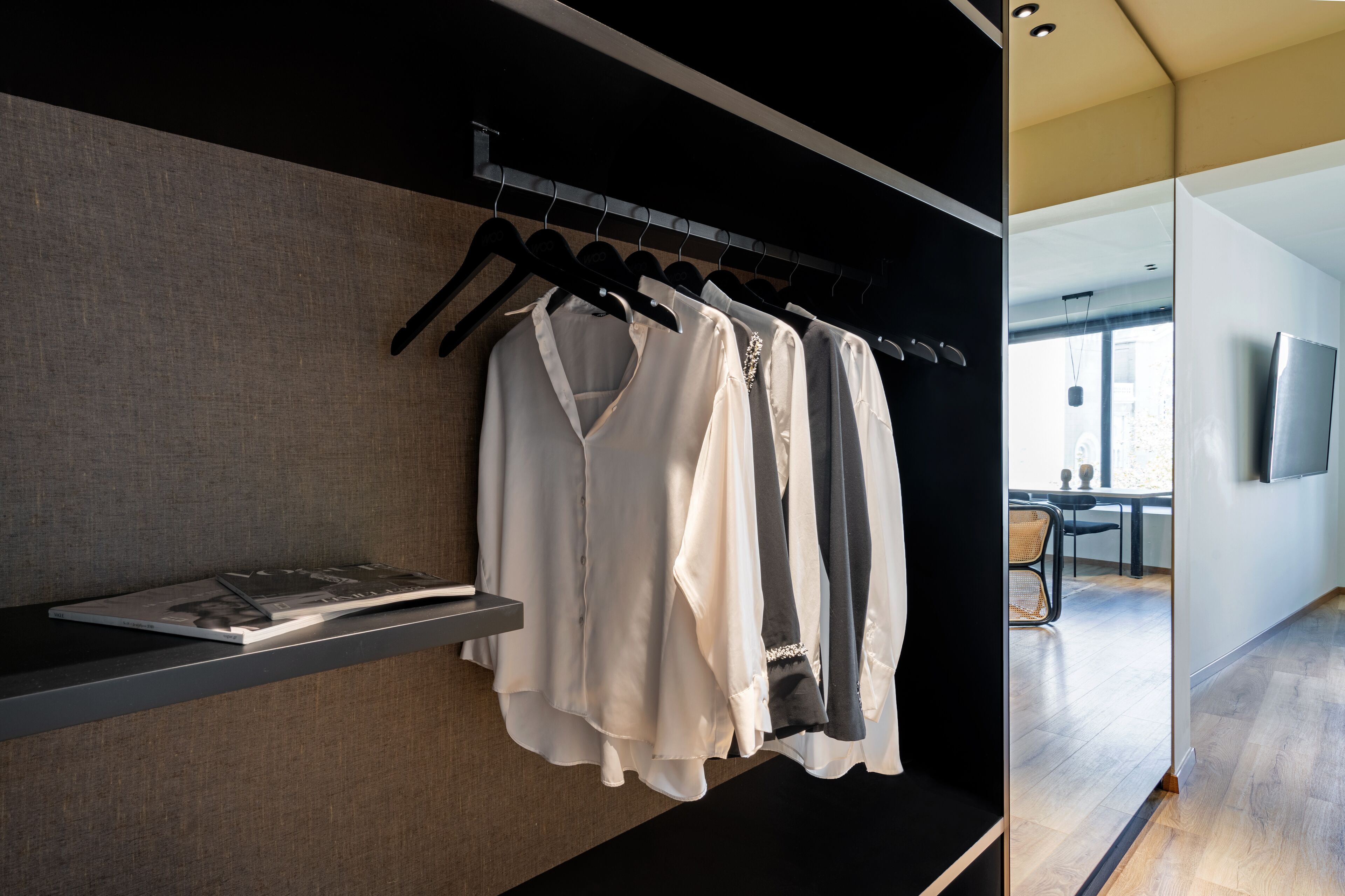 A modern hotel room with a clothing rack, a flat-screen TV, and a wooden floor.