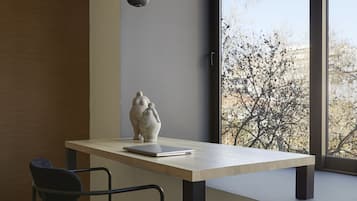 Une pièce moderne avec un plancher en bois, une chaise sombre, une table ornée d’un vase et une grande fenêtre donnant sur des arbres.