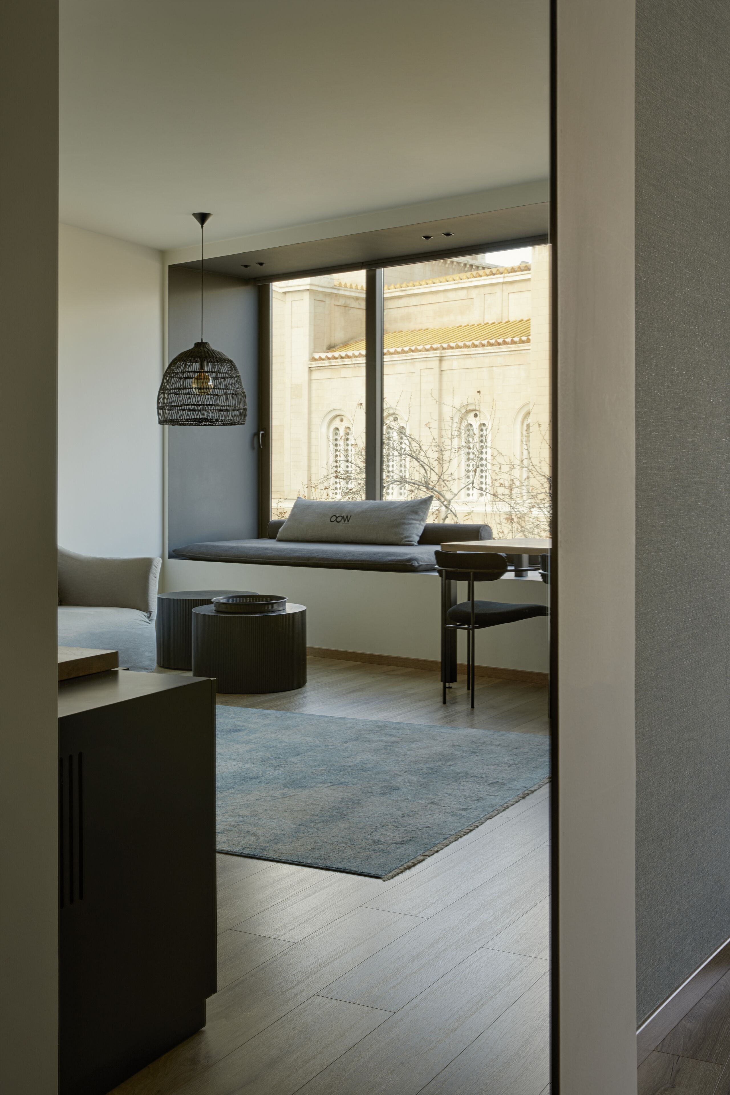 A modern living room with a large window, a sofa, a table, and a hanging light fixture.