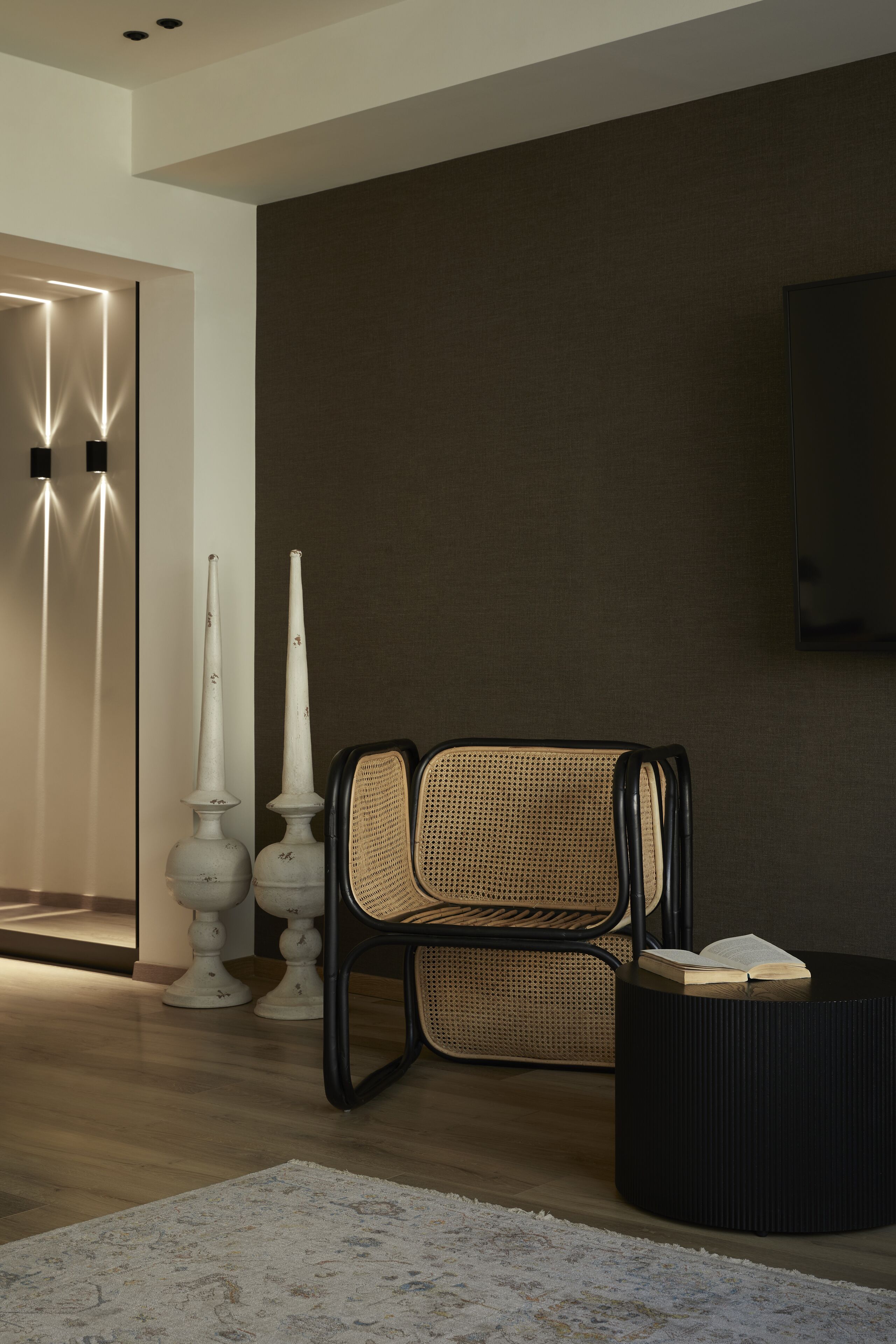 A modern living room with a black upholstered chair, a round black side table, and a large wall-mounted TV.