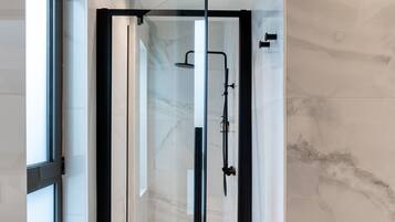Un baño moderno con ducha de vidrio, paredes de mármol y un ventanal amplio.