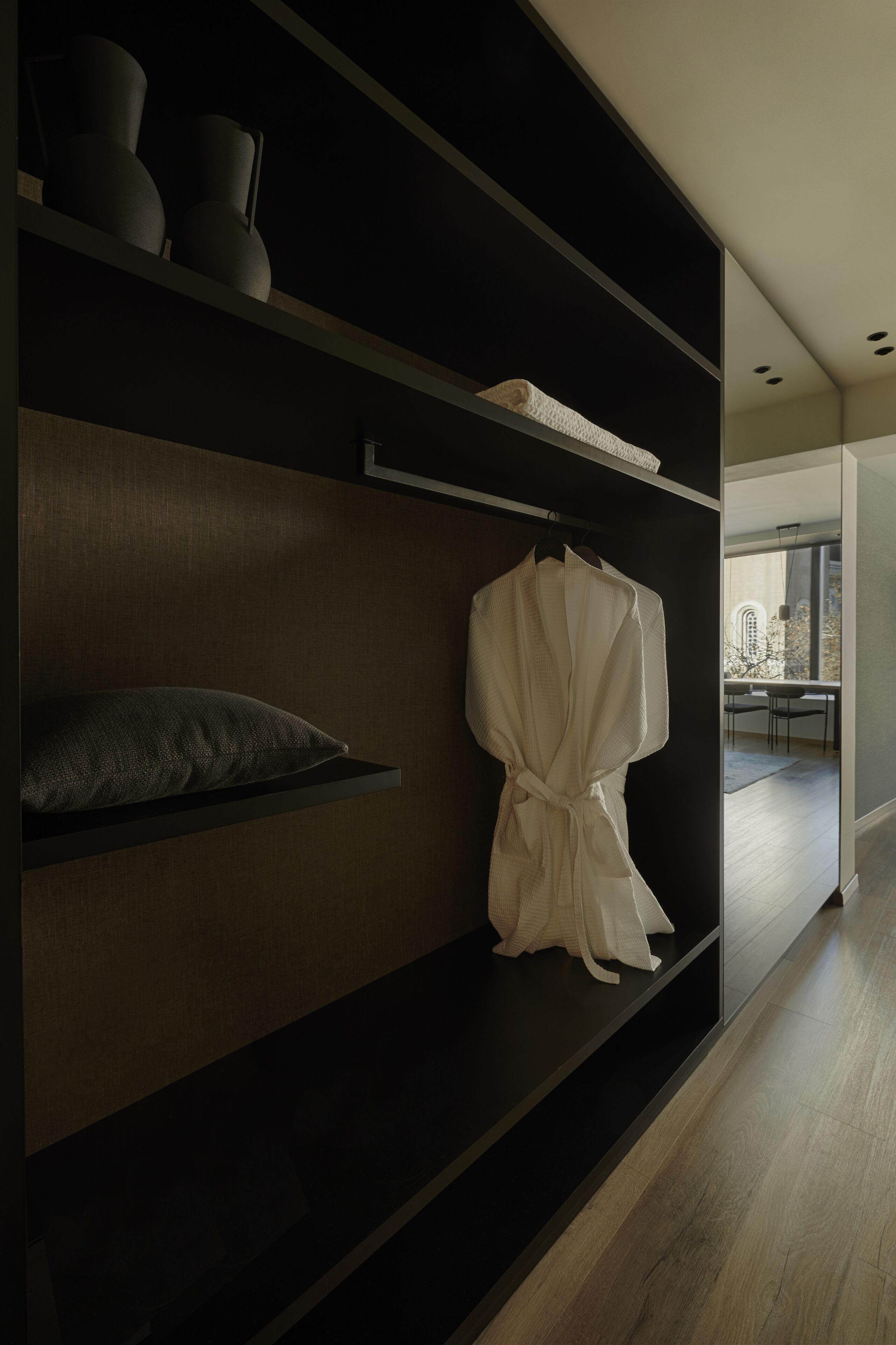 A modern interior with a dark wood shelving unit, a white robe hanging, and a view of a dining area through a glass door.