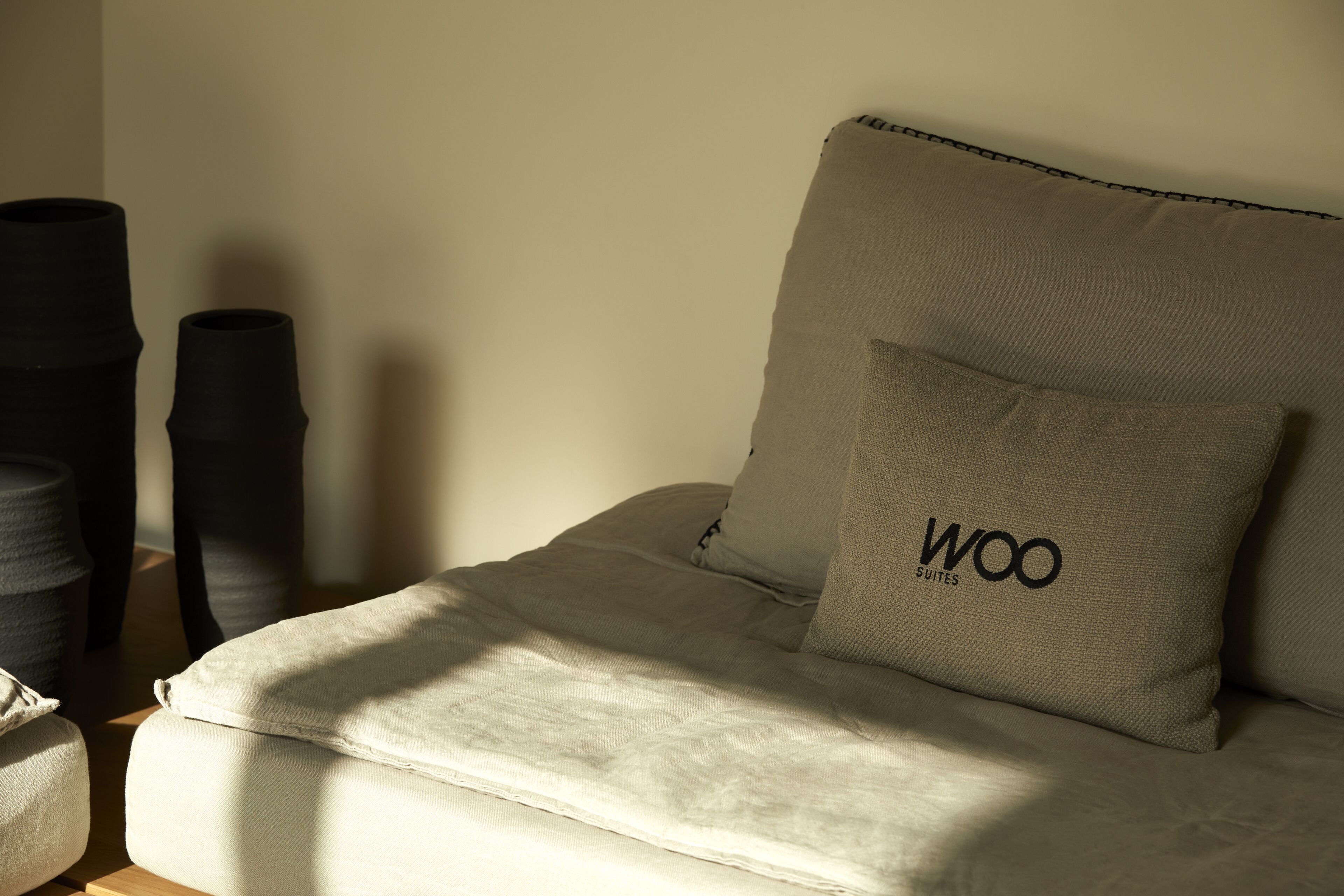 Una cama con un almohadón que dice "Woo Suites" y una mesita de noche con una lámpara.