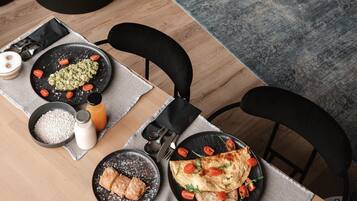 Comedor con mesa de madera dispuesta para dos, con platos de comida, una jarra de jugo y un tazón de arroz.