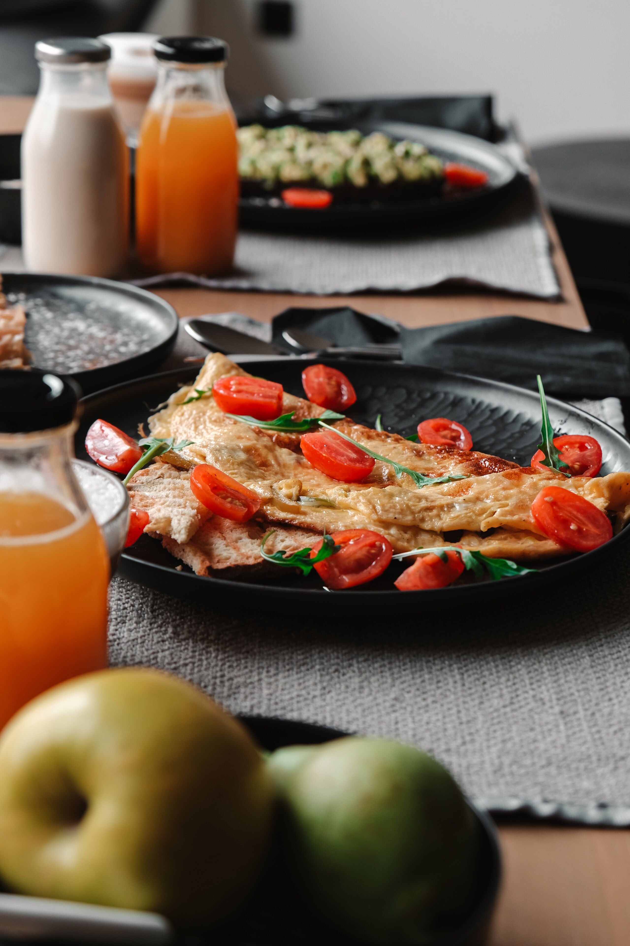 A meal with fish, tomatoes, and greens on a plate, with a bottle of juice and a pitcher in the background.
