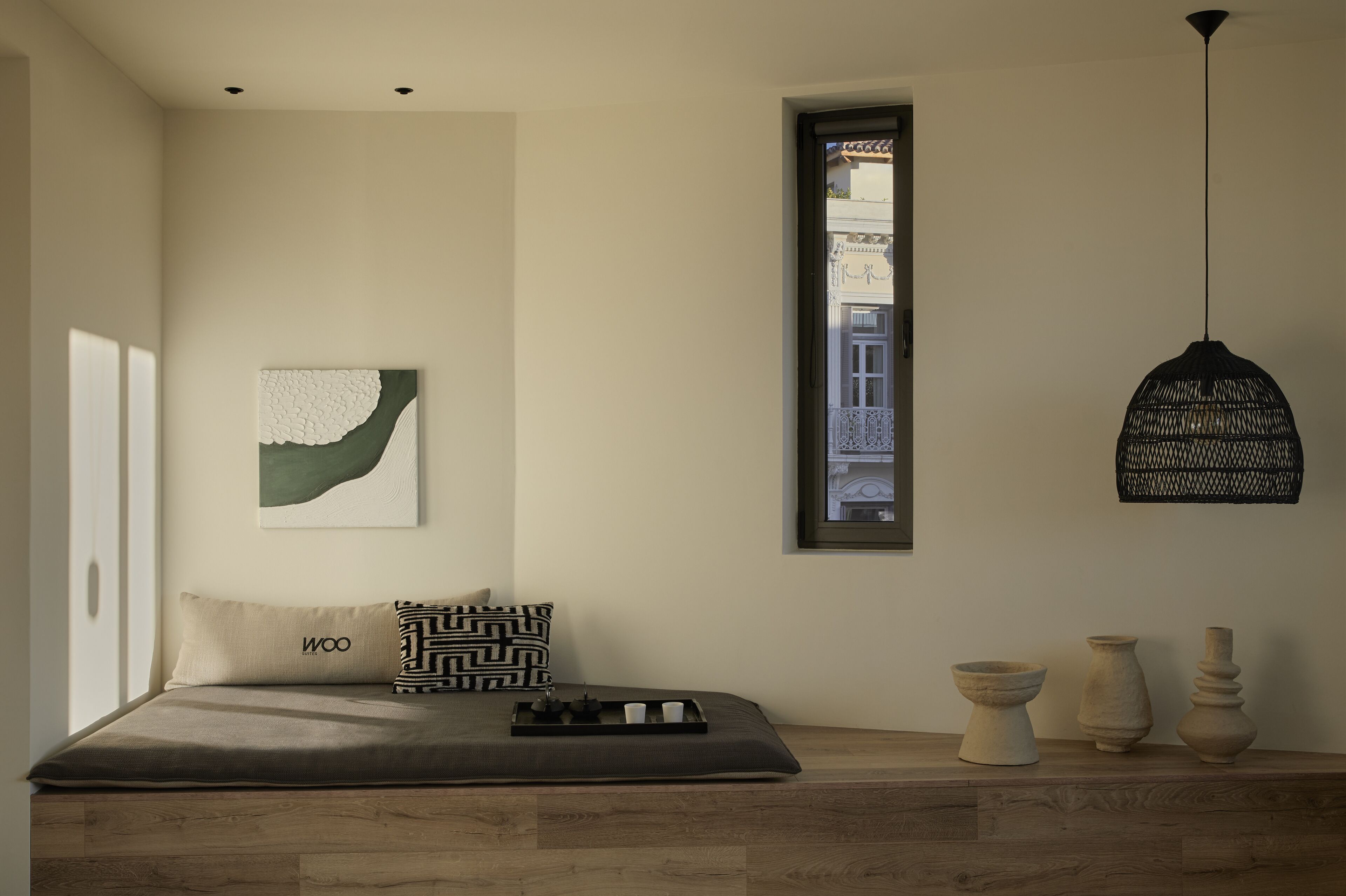 Een minimalistisch slaapkamer met een bed, een raam, een hanglamp en een klein plankje met decoratieve spullen.