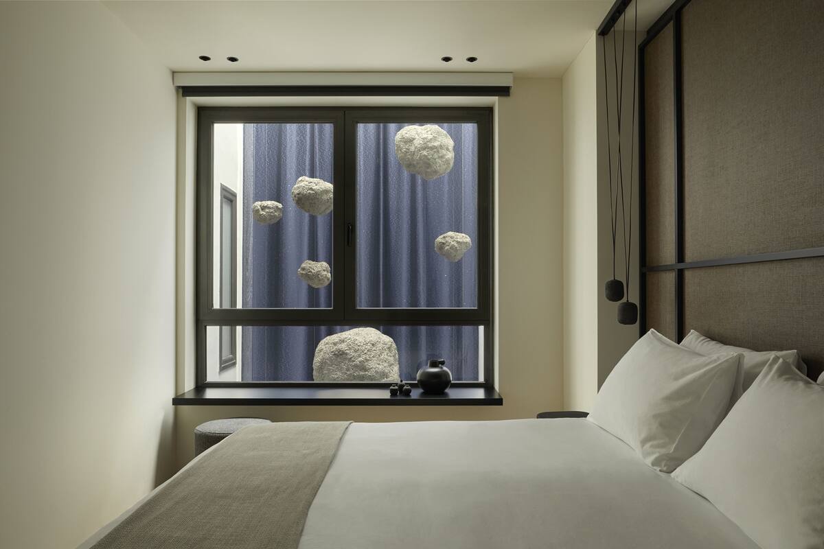 A bedroom with a large bed, a window with curtains, and a bedside table with a vase.