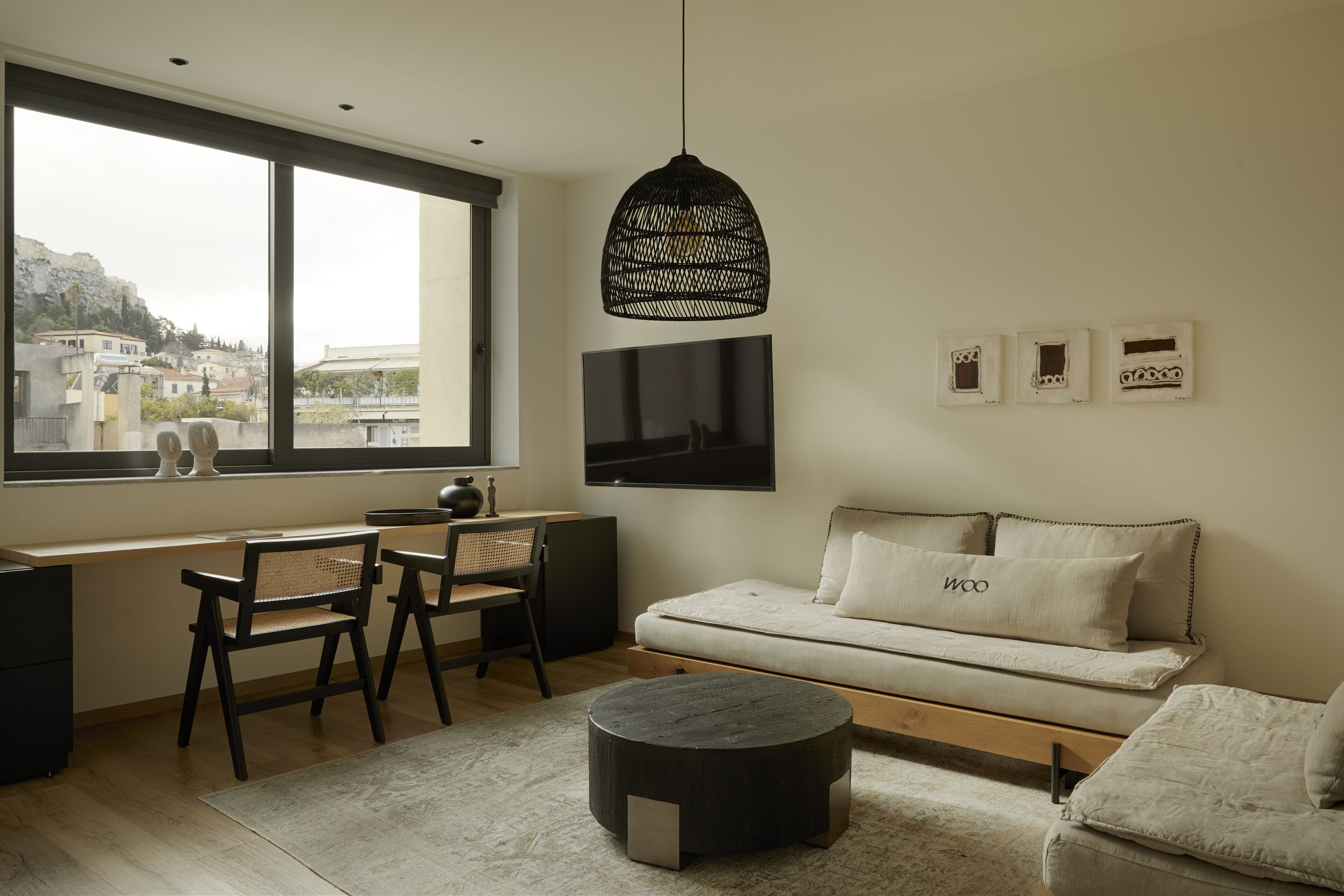 A modern living room with a large window, a black hanging light fixture, a flat-screen TV, and a sofa with a cushion labeled "woo".