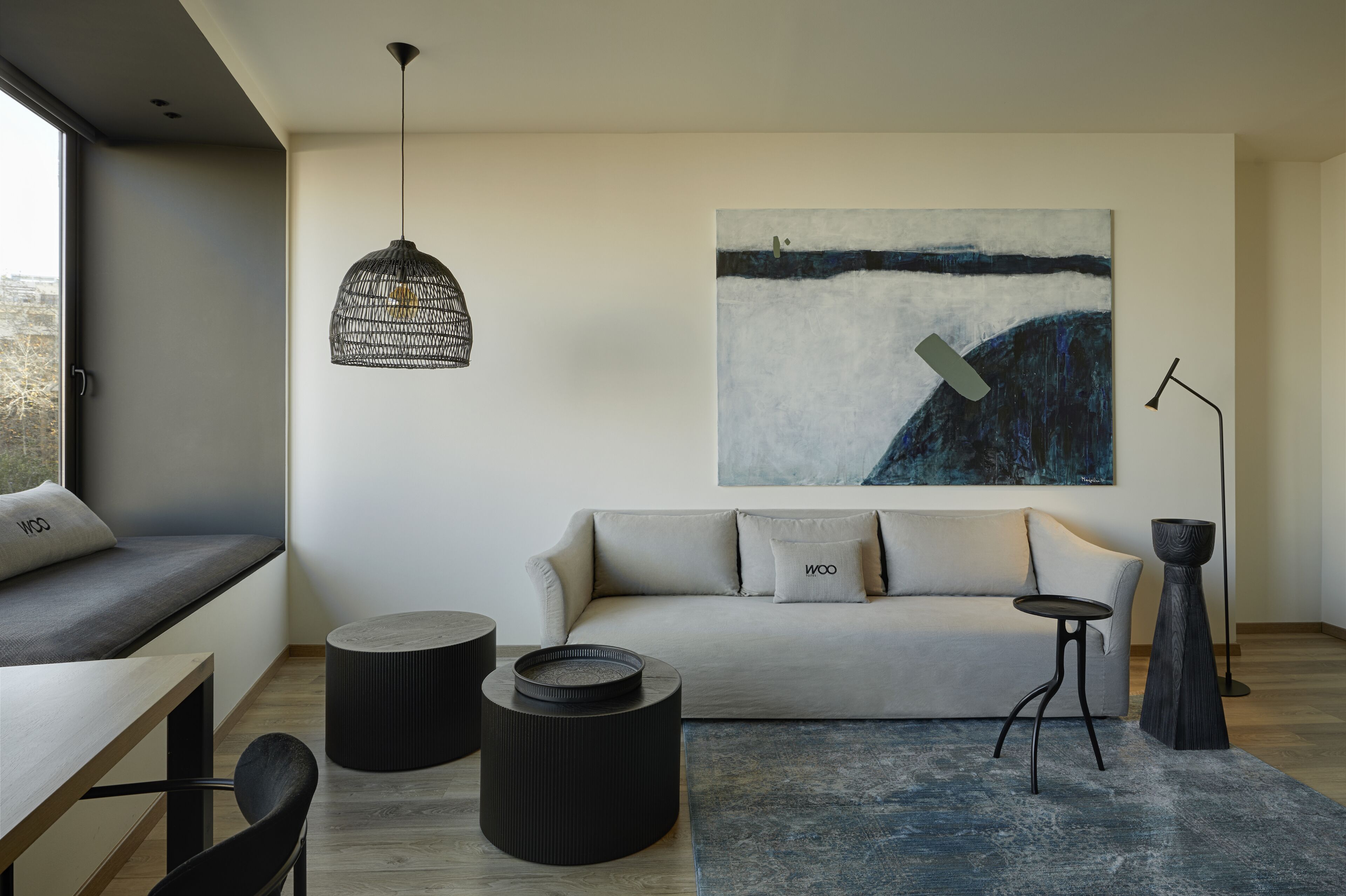 Una sala de estar moderna con un sofá, mesas auxiliares redondas negras, una lámpara colgante de tejido y un cuadro abstracto grande en la pared.