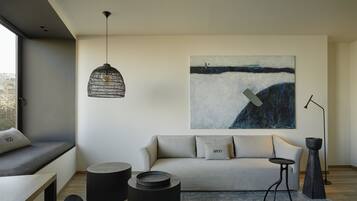 Una sala de estar moderna con un sofá, mesas auxiliares redondas negras, una lámpara colgante de tejido y un cuadro abstracto grande en la pared.