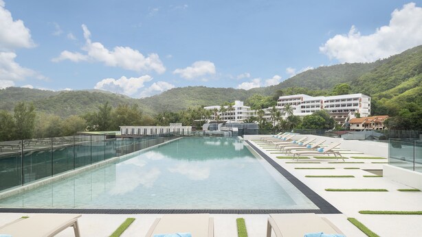 A swimming pool with lounge chairs and a view of a hillside building. - JonoX Phuket Karon Hotel (Karon)
